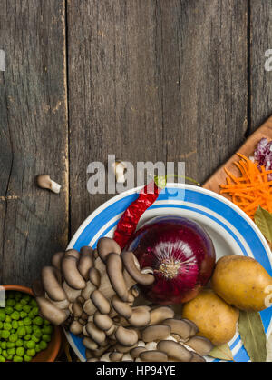 Ingredienti per la zuppa di verdure. verdure cetriolo cipolle patate carote funghi piselli spezie nella sezione sul grigio Sfondo di legno Foto Stock