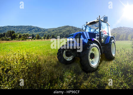 Blue generic trattore agricolo su un prato verde alla luce del sole. Foto Stock