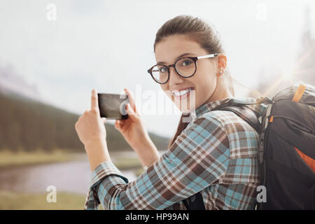 Giovane donna sorridente gite nella natura sulle montagne e scattare foto con il suo touch screen smartphone Foto Stock