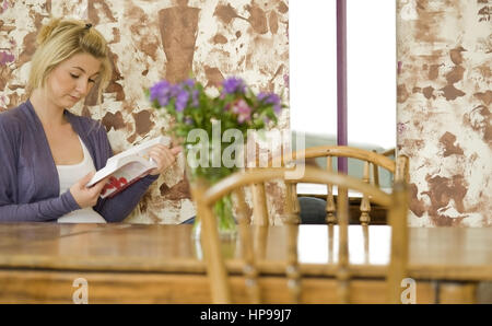 Modello rilasciato , Junge Frau, 24, sitzt am Tisch und liest ein Buch - donna la lettura di un libro Foto Stock