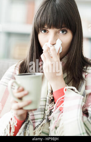 Malata a casa con raffreddore e influenza, ella si soffia il naso e avente una bevanda calda Foto Stock