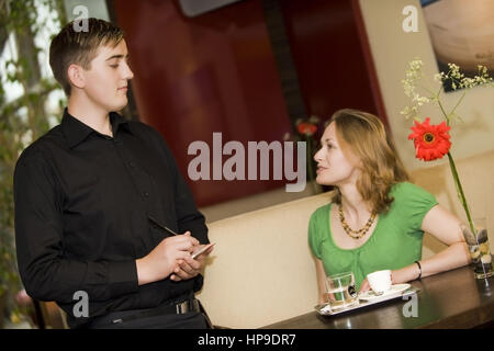 Modello rilasciato , Kellner bedient junge Frau im Kaffeehaus - in cafe Foto Stock