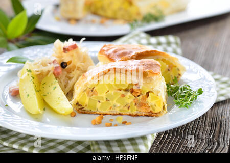 Sostanziosa cucina austriaca: strudel di patate con ciccioli, servita con crauti e pancetta Foto Stock