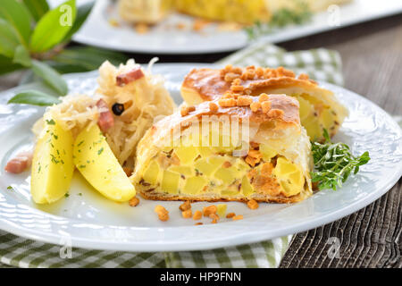 Sostanziosa cucina austriaca: strudel di patate con ciccioli, servita con crauti e pancetta Foto Stock