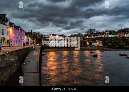 Portree Harbour, Isola di Skye in Scozia al crepuscolo. Febbraio 2017, mostra gli edifici al crepuscolo come le luci si accendono, impostare contro scure nuvole drammatico. Foto Stock