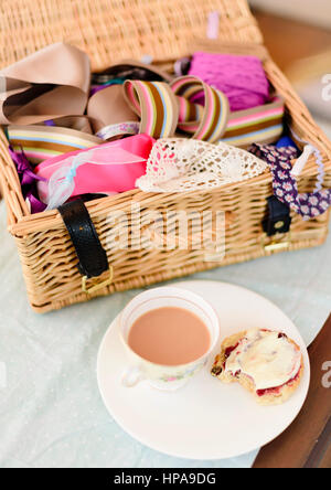 Tè alla crema. Tazze di tè e scones con marmellata e clotted cream accompagnato da un cesto di vimini riempito con tessuto Foto Stock