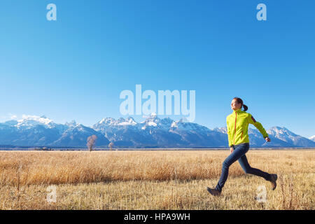 Felice giovane donna corre su un prato al tramonto, Grand Teton mountain range in distanza, il Parco Nazionale del Grand Teton, Wyoming negli Stati Uniti. Foto Stock