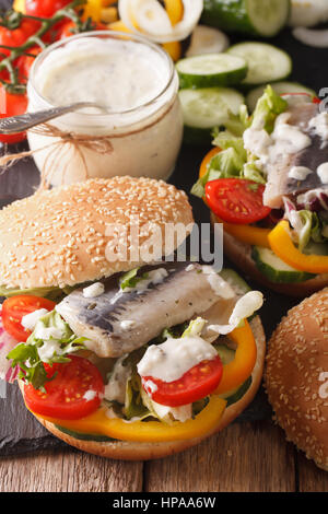 Hamburger di pesce con marinata di aringhe, con sugo di carne e verdura fresca vicino sul tavolo. In verticale Foto Stock