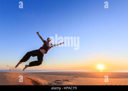 Giovane uomo felicemente di salto in aria, tramonto, Namib Desert, Langstrand, Swakopmund, Regione di Erongo, Namibia Foto Stock