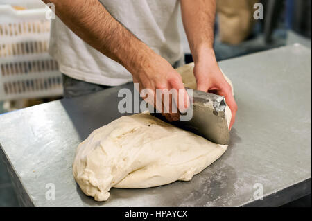 Close-up baker maschio mani taglio pezzo di pasta con il vecchio impasto coltello raschiatore su panetteria di metallo la superficie del tavolo Foto Stock