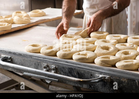 Close-up baker maschio mani rendendo frisella italiano ciambelle di pane, ponendo impasto crudo sulla tavola da forno Foto Stock