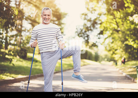 Attività piacevole. Gioiosa bella età azienda man walking e di esercizio durante la pratica del Nordic walking Foto Stock