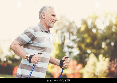 Mi piace lo sport. Allegro lieto uomo anziano sorridente e facendo qualche attività sportiva pur essendo al di fuori Foto Stock