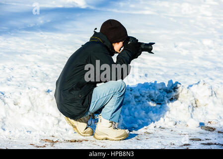 I giovani adulti fotografo inginocchiato in ambiente invernale per scattare una foto. Foto Stock