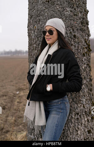 Bella caucasico svedese moda ragazza in piedi all'aperto nel paesaggio invernale. Indossare il jeans, camicia, sciarpa e cappello e occhiali da sole Foto Stock