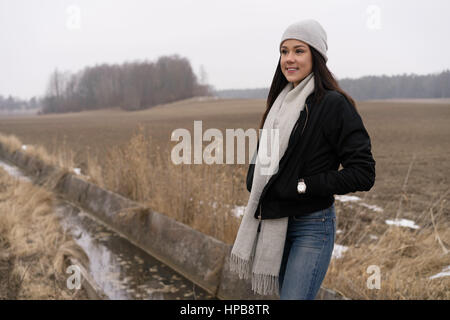 Bella caucasico svedese moda ragazza in piedi all'aperto nel paesaggio invernale. Indossare il jeans, camicia, sciarpa e cappello Foto Stock