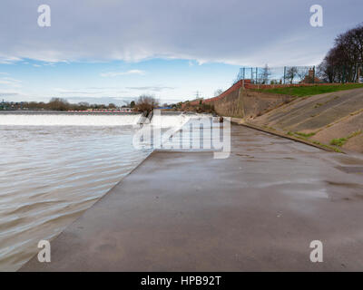 Un calcestruzzo pendenza conduce a uno stramazzo sulle rive di un fiume Foto Stock