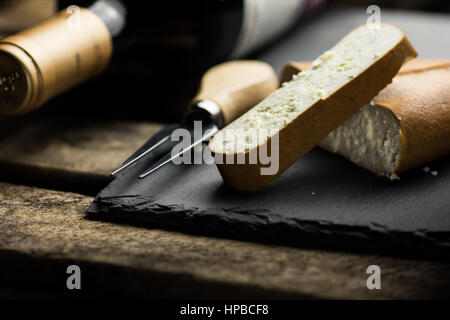 Frammento e di spessore fetta tagliata affumicato di formaggio di capra con la forcella della pietra nera bordo, bottiglia di vino, cena gourmet, close up Foto Stock