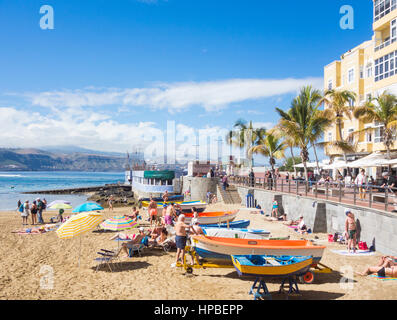 La gente a prendere il sole vicino colorate barche da pesca a La Puntilla sulla spiaggia di Las Canteras a Las Palmas di Gran Canaria Isole Canarie Spagna Foto Stock