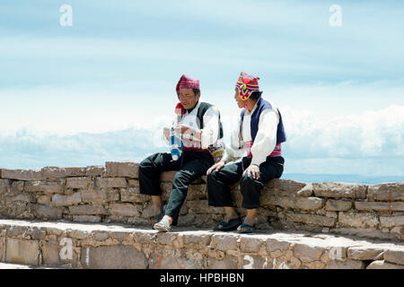 Due uomini vestiti in abiti tradizionali specifici per l'isola di Taquile regione, uno di loro la tessitura di un cappello. Il lago Titicaca, Perù - Ottobre 17, 2012 Foto Stock