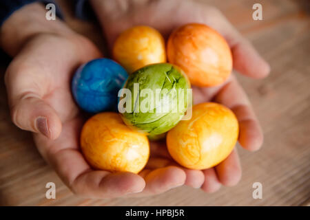 Caucasico maschio mani colorate le uova di Pasqua su sfondo di legno. Dipinto di uova nelle mani di un uomo su sfondo di legno Foto Stock