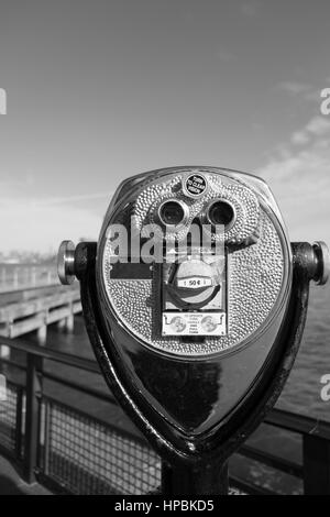 Il visualizzatore di torre binocolo su Liberty Island cercando verso Manhattan, New York. Pier e dello skyline di Manhattan in distanza. Bianco e nero, concentrarsi su Foto Stock