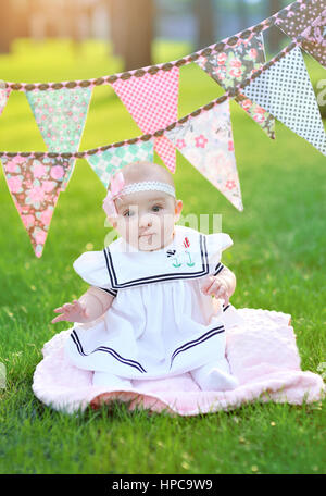 Bambina in abito bianco seduto sull'erba nel parco Foto Stock