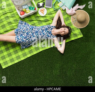 Giovane donna sorridente di relax all'aperto e avente un picnic, ella è sdraiato su un manto in erba Foto Stock