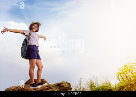 Felice escursionista asian teens carina ragazza con zaino cappello e occhiali sorridente permanente pone le braccia aperte sulla montagna e sullo sfondo del cielo di Phu Chi fa Forest Foto Stock