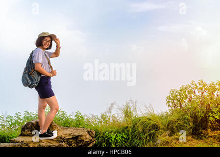 Tourist teens ragazza escursionista con zaino cappello e occhiali è sorriso permanente e pone felicemente in alta montagna su sky e lo sfondo di nebbia al punto panoramico Foto Stock