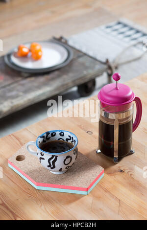 Una rosa cafetiere e una tazza di caffè nero di sedersi su un tavolo di legno Foto Stock