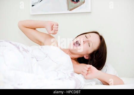 Modello rilasciato , Tagwache, Frau liegt gaehnend Bett im - donna gapeing nel letto Foto Stock
