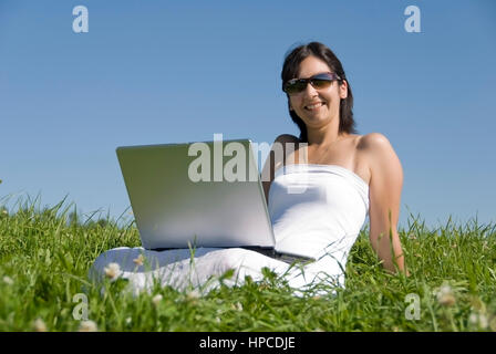 Modello rilasciato , Junge Frau sitzt mit Laptop in der Wiese - donna utilizzando laptop in Prato Foto Stock