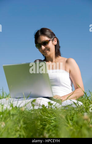 Modello rilasciato , Junge Frau sitzt mit Laptop in der Wiese - donna utilizzando laptop in Prato Foto Stock