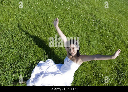 Modello rilasciato , Junge, glueckliche Frau sitzt in der Wiese und streckt Haende sie in die Hoehe - happy, giovane donna in Prato Foto Stock