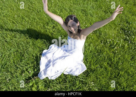 Modello rilasciato , Junge, glueckliche Frau sitzt in der Wiese und streckt Haende sie in die Hoehe - happy, giovane donna in Prato Foto Stock