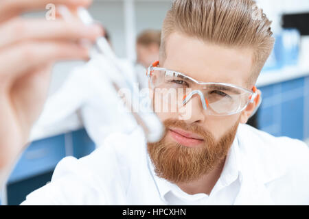 Vista ravvicinata del barbuto chimico in occhiali protettivi di ispezionare il tubo di test in laboratorio Foto Stock