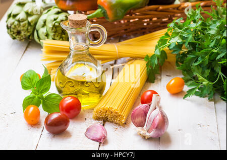 Italiano e cucina mediterranea ingredienti, spaghetti, olio d'oliva, aglio, pomodori, carciofi, peperoni dolci nel cestello sul tavolo da cucina, esterni Foto Stock