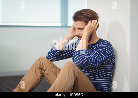 Triste business executive seduta contro la parete in ufficio Foto Stock