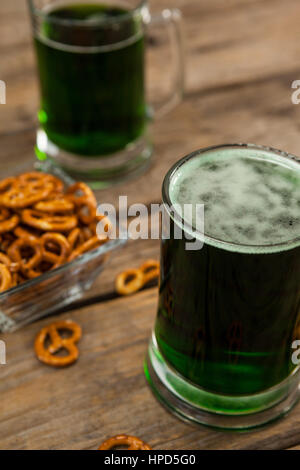 Il giorno di San Patrizio due boccali di birra verde con pretzel su una superficie di legno Foto Stock