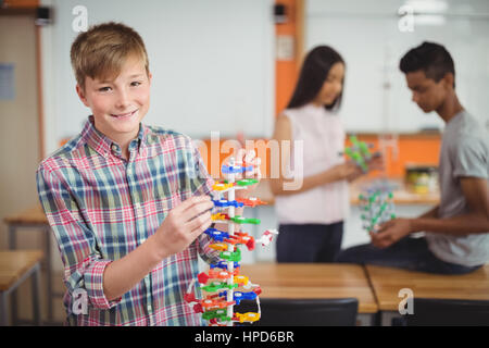 Ritratto di sorridere schoolboy esaminare il modello di molecola in laboratorio a scuola Foto Stock