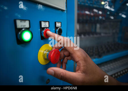 Le mani del lavoratore in fabbrica premendo un pulsante rosso sulla scheda di controllo in fabbrica Foto Stock