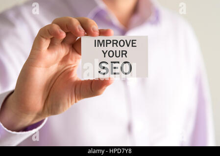 Primo piano su imprenditore tenendo una scheda con il testo di migliorare il tuo SEO, business Concetto di immagine con messa a fuoco morbida dello sfondo Foto Stock