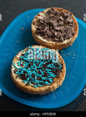 Due biscotti con cioccolato colorato spruzza su una piastra di colore blu Foto Stock