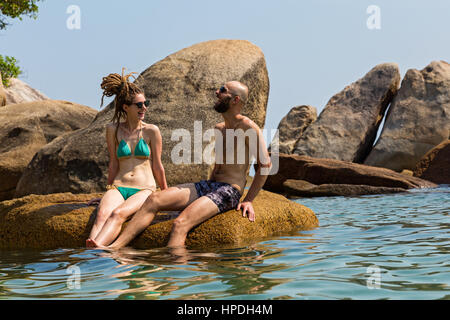 Allegro giovane seduto su una grossa pietra in mare Foto Stock