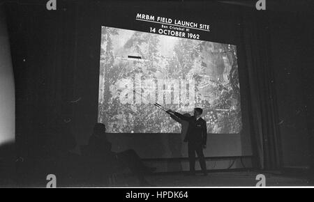 Uomo con puntatore davanti la proiezione di una diapositiva che mostra una foto aerea etichettato "Campo RBM Sito di lancio di San Cristobal #1 14 ottobre 1962,' alla discussione su Cuba al Dipartimento di Stato, Washington, DC, 10/14/1962. Foto Stock