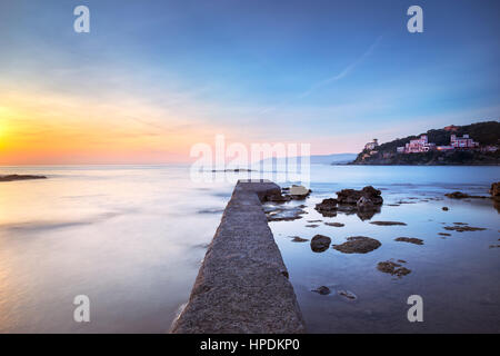 Castiglioncello destinazione di viaggio, molo di cemento nella baia, rocce a picco sul mare e sul tramonto. Toscana, Italia, Europa. Esposizione lunga Foto Stock
