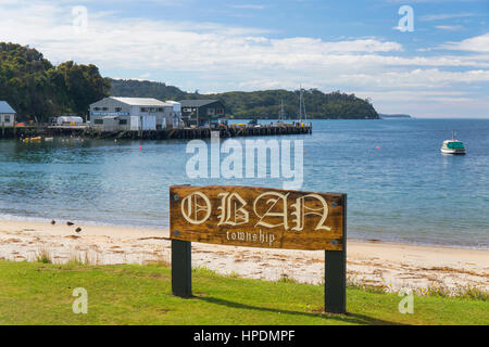 Oban, Isola Stewart, Southland, Nuova Zelanda. Scolpiti cartello in legno sulla riva di Halfmoon Bay. Foto Stock