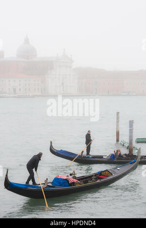 Due gondolieri sono visto avvicinarsi l'entrata dell'ormeggio a Piazza San Marco in una nebbiosa giornata a Venezia. Cimitero di San Michele può essere visto in t Foto Stock