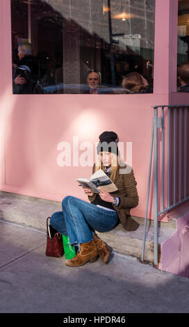 Elegante giovane donna leggendo una copertina rigida libro mentre in attesa di un tavolo in un ristorante Foto Stock